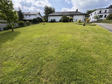 Sonniges Baugrundstück in ruhiger Wohnlage von Iserlohn, umgeben von Grün, mit Bäumen und Nachbarhäusern im Hintergrund