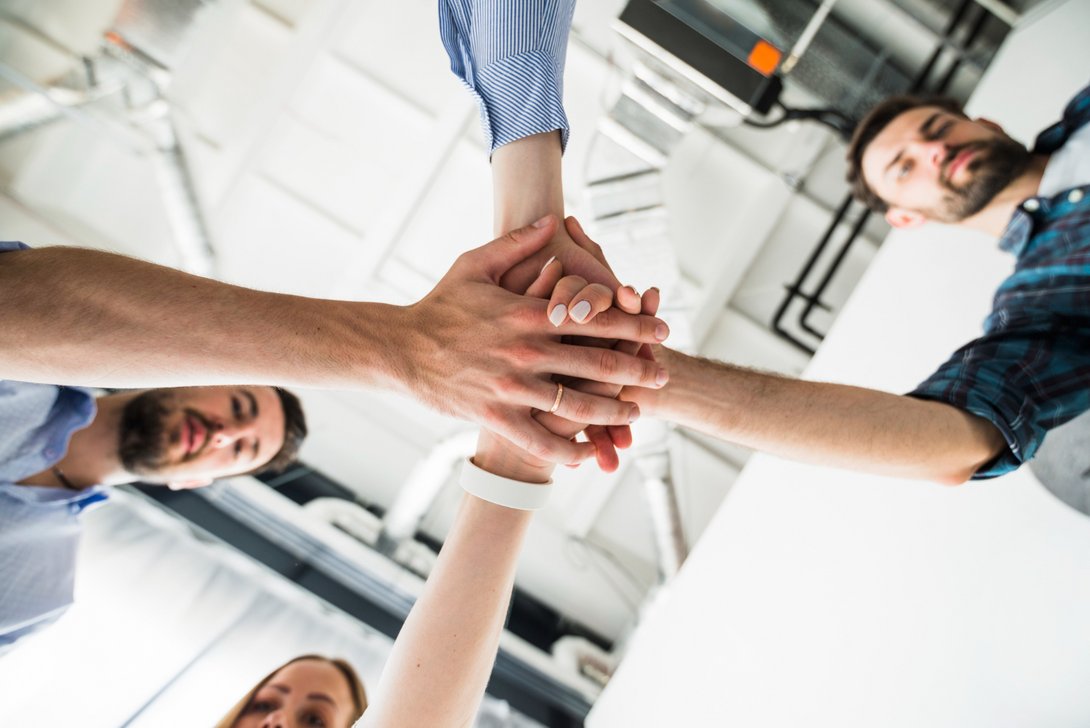 Hände von drei Personen, die sich in der Mitte treffen – Symbol für Zusammenarbeit und Partnerschaft